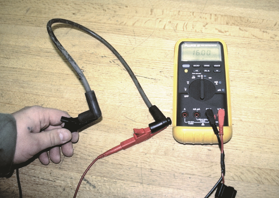 Measuring the resistance of a spark  plug wire with a multimeter set to the ohms position.  The ...