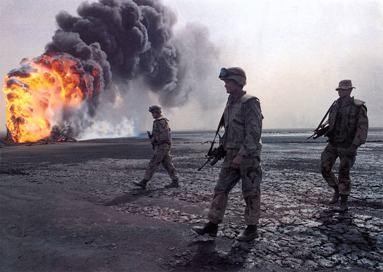 American soldiers advance past a burning oil well. As the routed Iraqi army fled Kuwait, it ignited ...